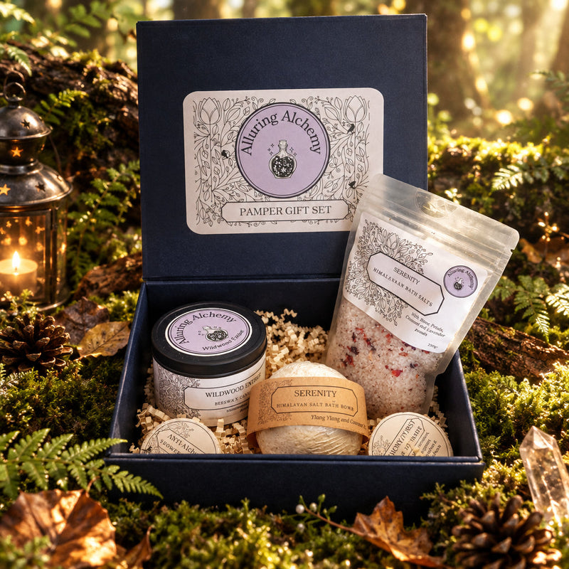 An open dark black gift box on a forest floor containing a jar, a wrapped bath product, and bath salts, with a visible Allington Alchemy label on the lid and front of the items.
