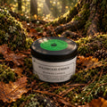 Beeswax candle labeled 'Wildwood Ember' on a natural background with greenery.