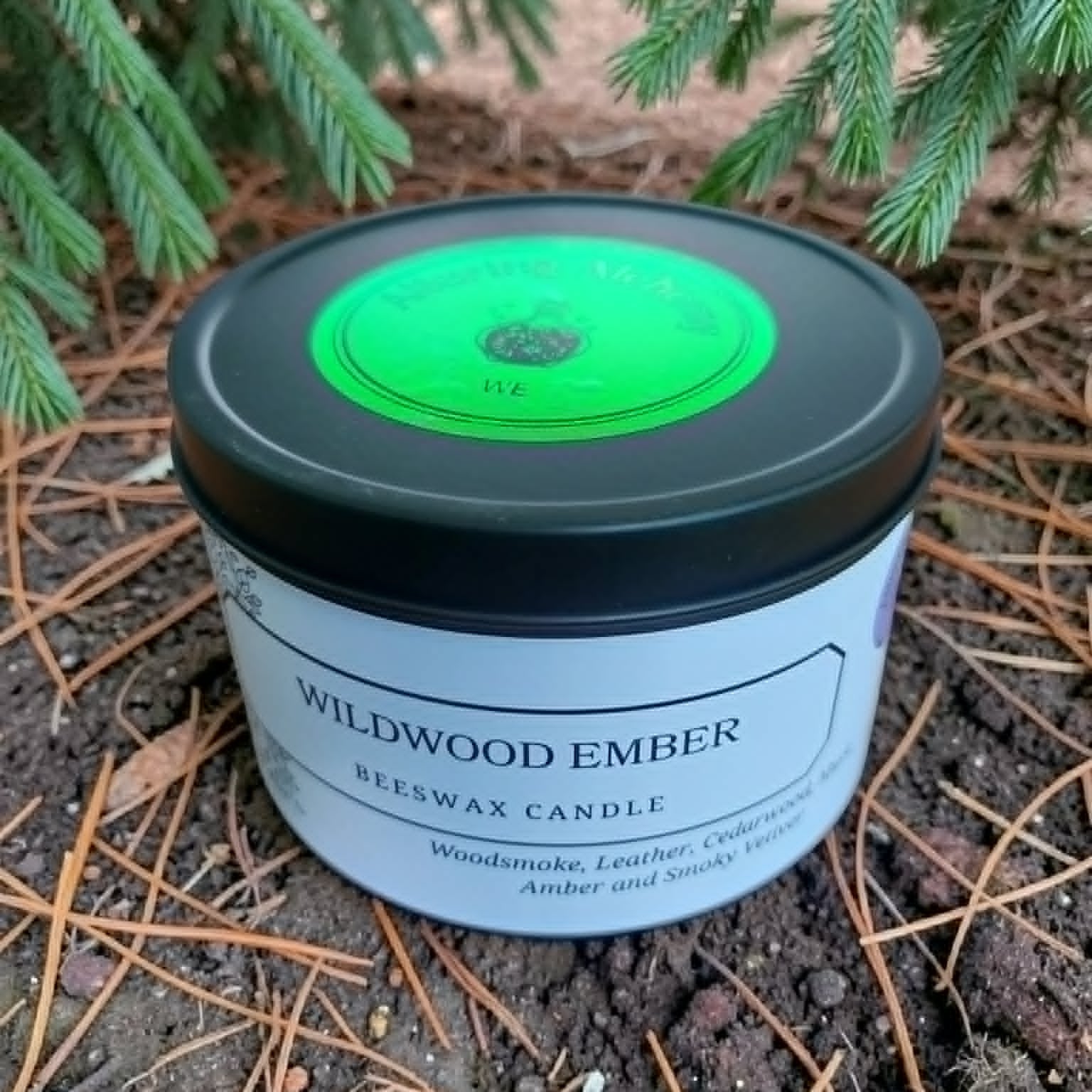 Beeswax candle labeled 'Wildwood Ember' on a natural background with greenery.