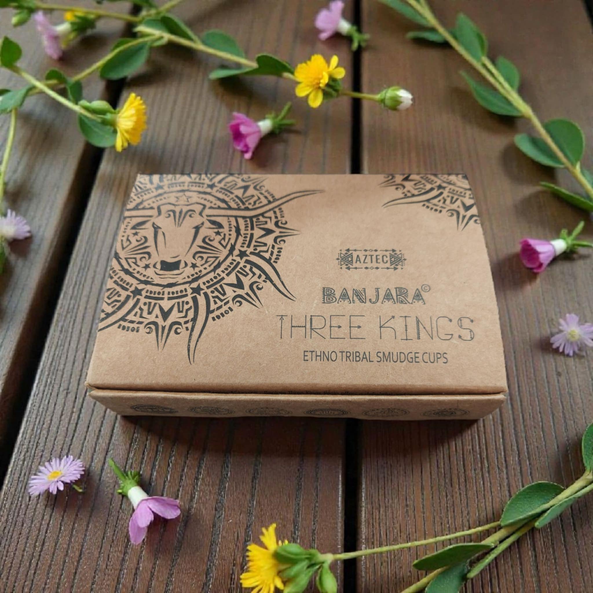 Brown box with tribal design and text on a wooden surface with flowers