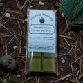 Pack of Alluring Alchemy Evergreen Hush wax melts on a natural background with pine needles and twigs.