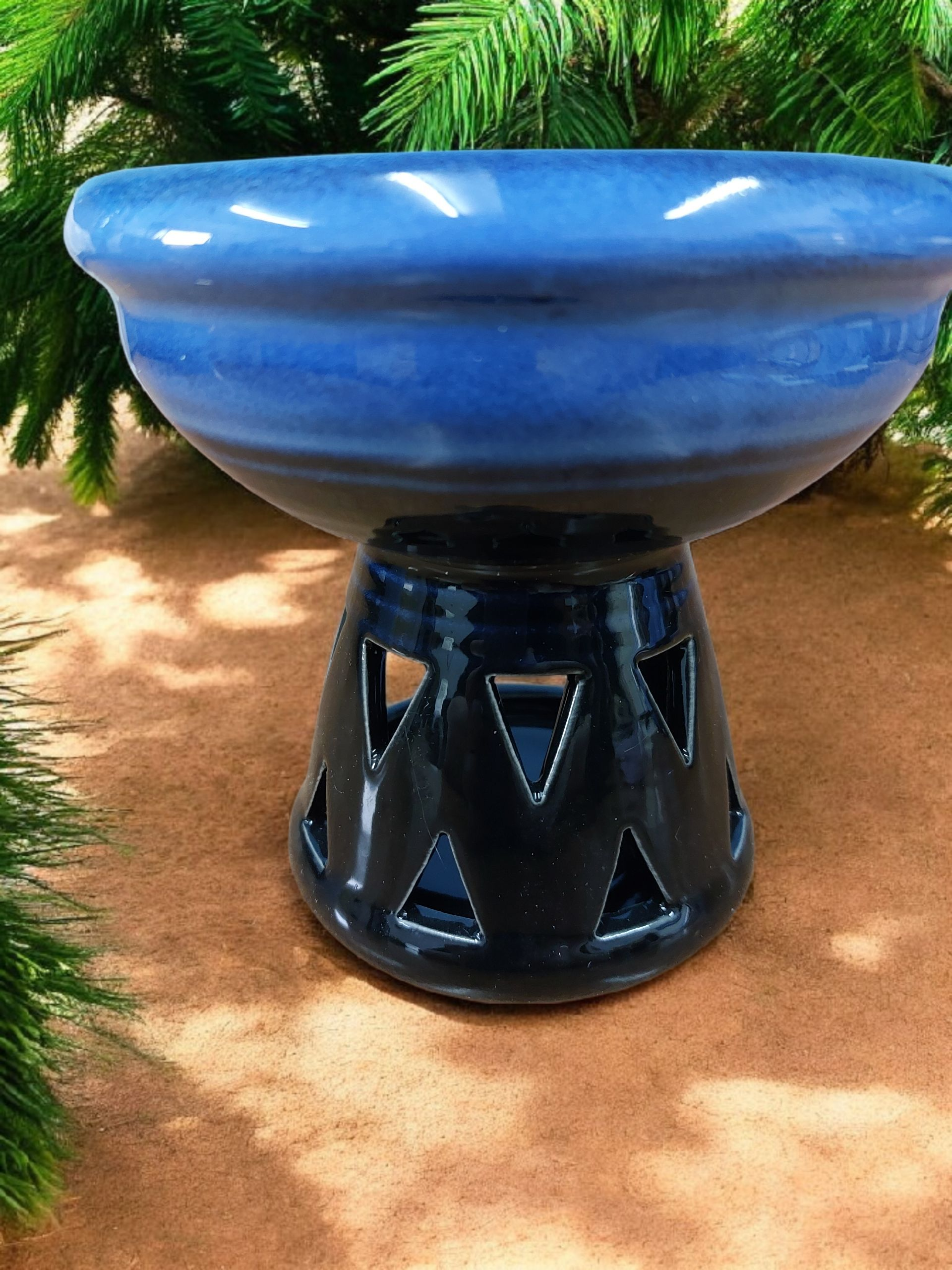 Blue ceramic bowl on a black stand with greenery in the background