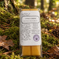 A packaged beeswax wax melt bar labeled 'Citrus Ember' resting on a light wood surface. The product has a white paper label with black botanical line art and text, with yellow-orange wax visible at the top and bottom of the clear plastic wrapper.