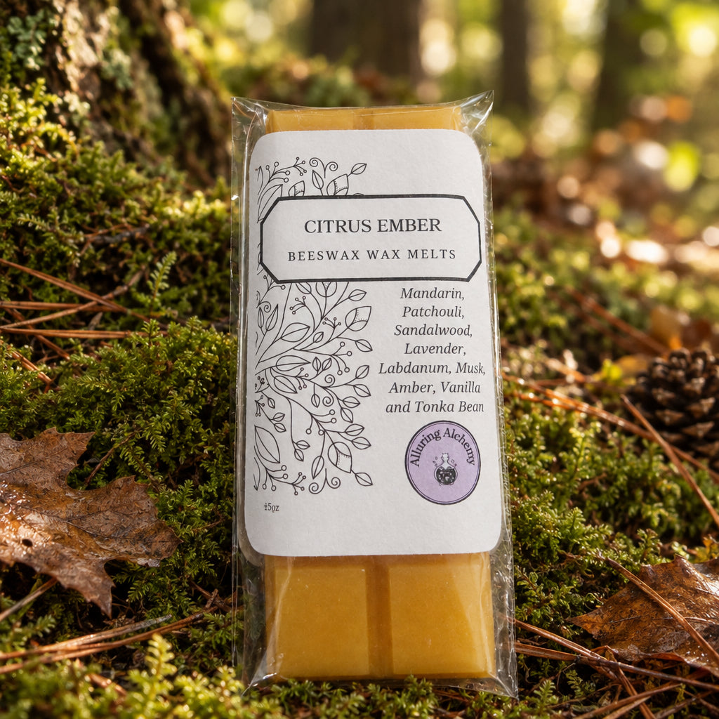 A packaged beeswax wax melt bar labeled 'Citrus Ember' resting on a light wood surface. The product has a white paper label with black botanical line art and text, with yellow-orange wax visible at the top and bottom of the clear plastic wrapper.