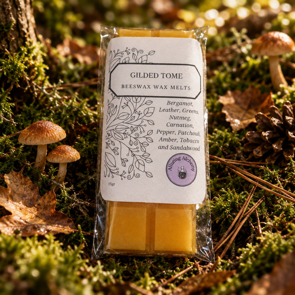 A packaged bar of beeswax melt labeled 'Gilded Tome' by The Queeny Academy, showing two yellow wax bars in clear plastic packaging on a light wood surface.
