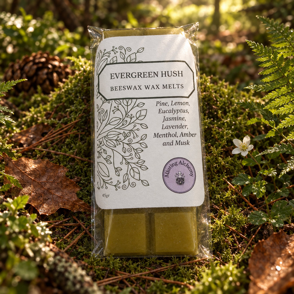 A packaged bar of beeswax wax melts labeled 'Evergreen Hush' by Alluring Alchemy, sitting on a light wood surface. The product consists of a white paper label with black text and illustrations, and two yellow-green beeswax bars visible at the bottom.