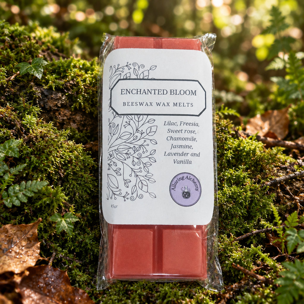 A package of Enchanted Bloom Beeswax Wax Melts in 'Enchanted Bloom' scent, featuring two orange-red wax bars in a clear plastic sleeve with a white label, placed on a light wood grain surface.