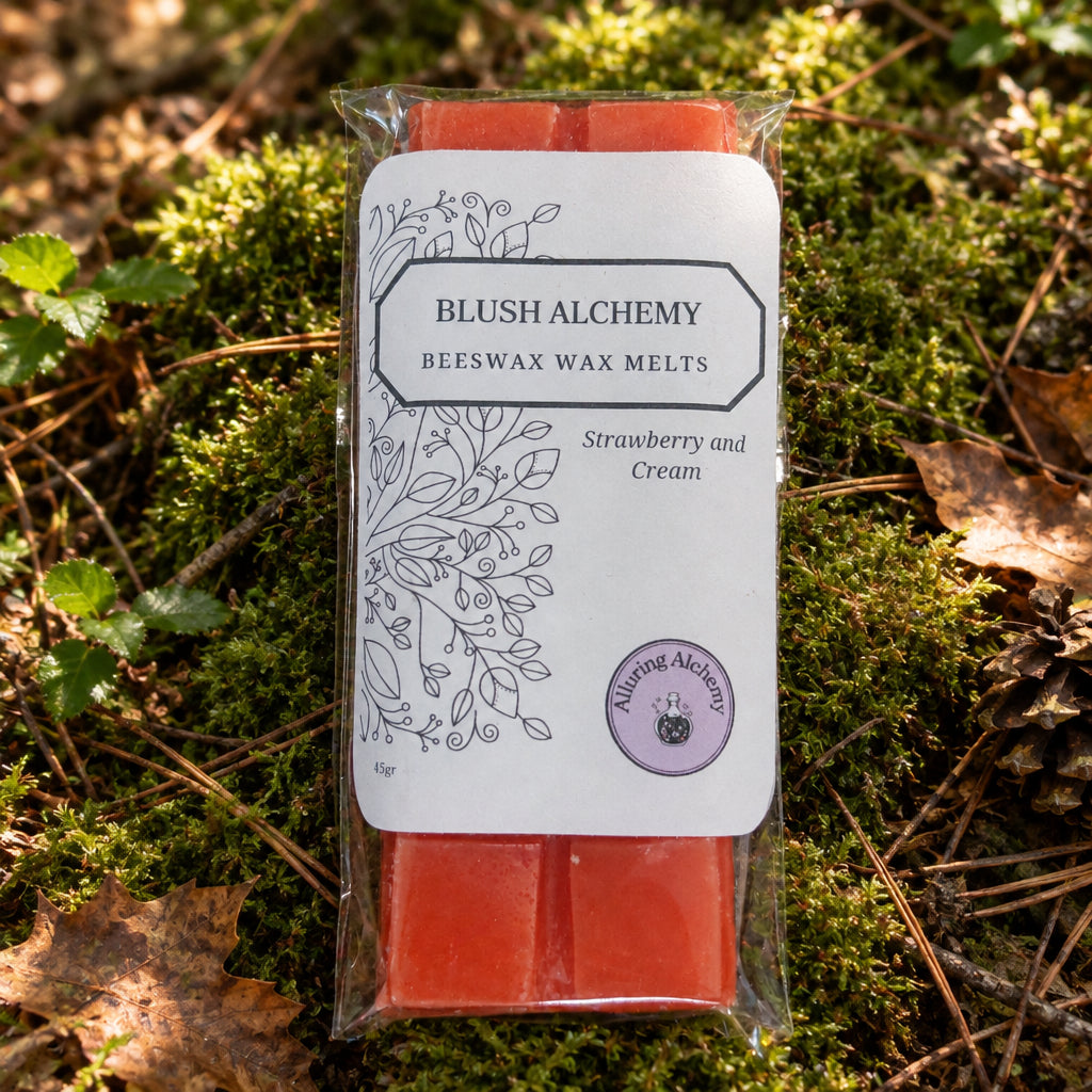 A packaged bar of wax melt from Blush Alchemy, labeled 'Strawberry and Cream', showing the orange wax at the top and bottom of a clear plastic wrapper on a light wood background.