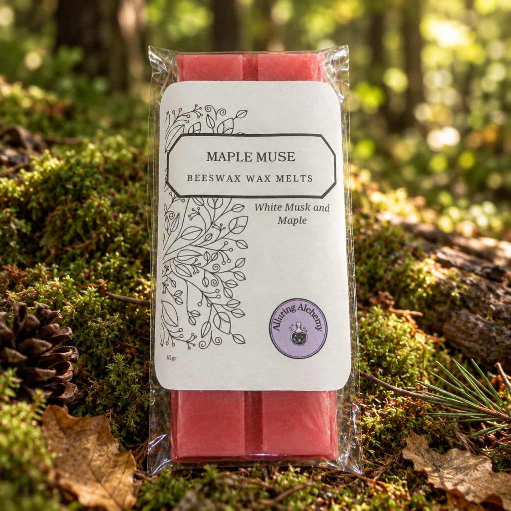 A packaged bar of Maple Muse Beeswax Wax Melts, showing the pink wax bar through a clear plastic sleeve with a white paper label, placed on a light wood grain surface.