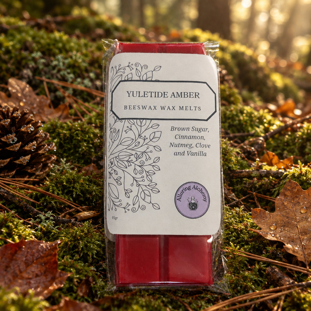 A packaged bar of Yuletide Amber beeswax wax melts by Alluring Alchemy, resting on a light wood grain surface. The wax melt is red, visible through clear plastic packaging with a white paper label.