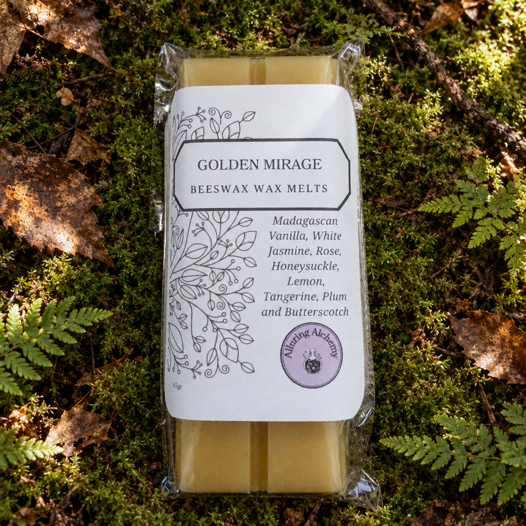 A packaged bar of Golden Mirage Beeswax Wax Melts on a forest floor. The product is in clear plastic packaging with a white paper label featuring black text and botanical line art, and a small purple circular logo.