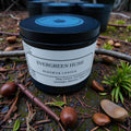 Beeswax candle labeled 'Evergreen Hush' surrounded by natural elements on a rustic background