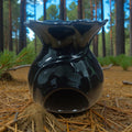 Black ceramic oil burner on pine needles with a forest background