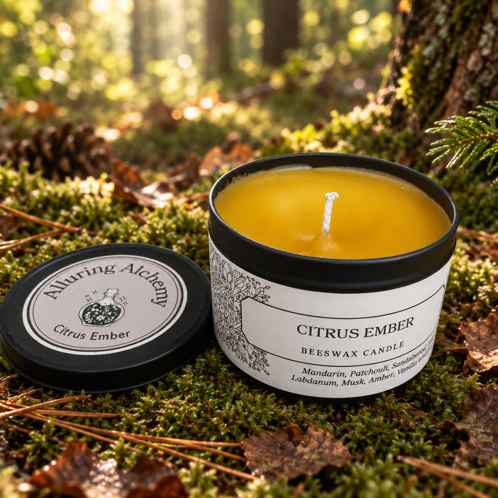 A lit citrus amber beeswax candle in a black tin with a white label sits on forest floor
