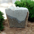 Bar of soap with a natural, earthy coloration on a textured surface with greenery in the background
