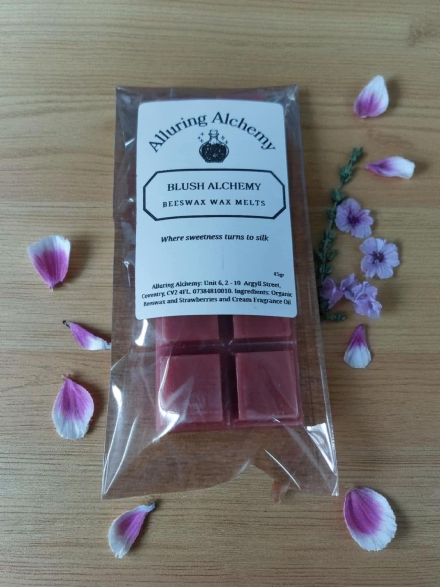 Packaged wax melts from Alluring Alchemy with pink petals and flowers on a wooden surface