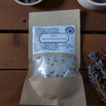 Packaged Himalayan bath salts with two bowls of purple and gray substances on a wooden surface.