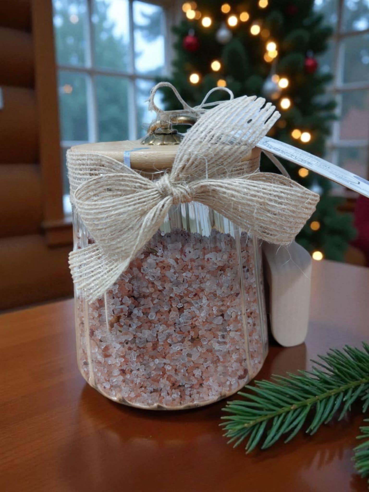 Jar of bath salts with a decorative bow on a wooden surface, Christmas tree in the background