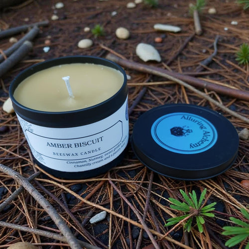 Amber Biscuit candle with a black lid on a natural background of twigs and pine needles.