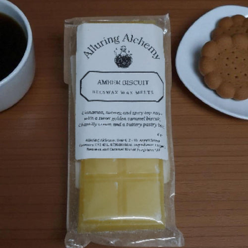 Packaged amber biscuit with a label on a wooden surface next to a cup of coffee and a plate of cookies.
