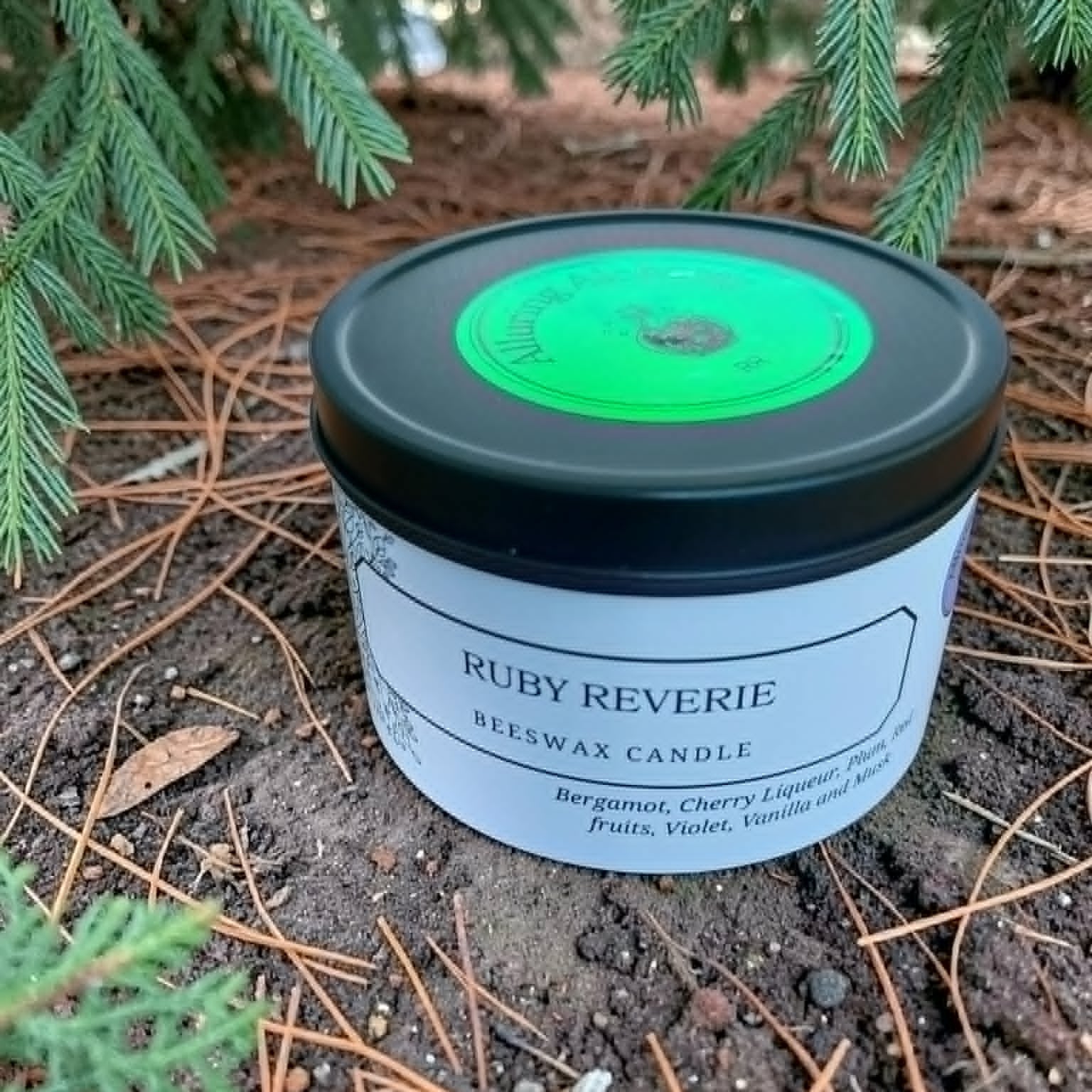 Beeswax candle labeled 'Ruby Reverie' on a natural ground surface with greenery.