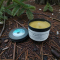 Beeswax candle labeled 'Pure Glow' on a natural setting with pine needles and branches.