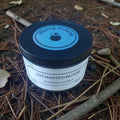 Beeswax candle jar labeled 'Enchanted Bloom' by Alluring Alchemy on a natural background.