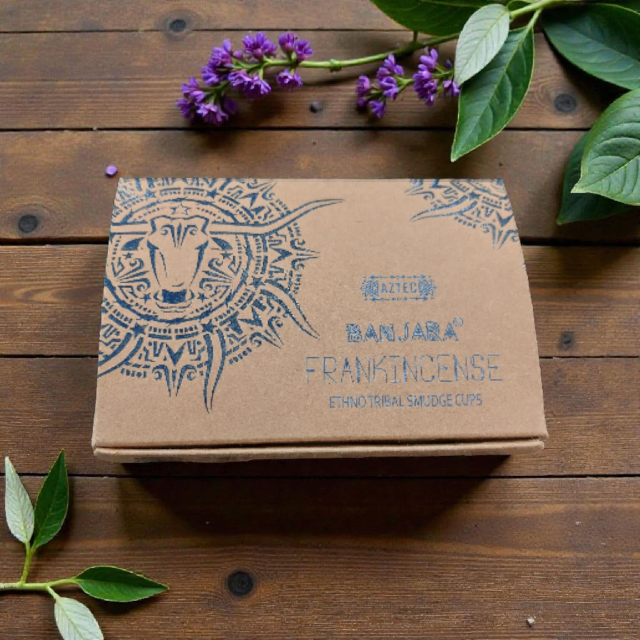 Brown cardboard box with decorative design and text on a wooden surface with purple flowers and green leaves.