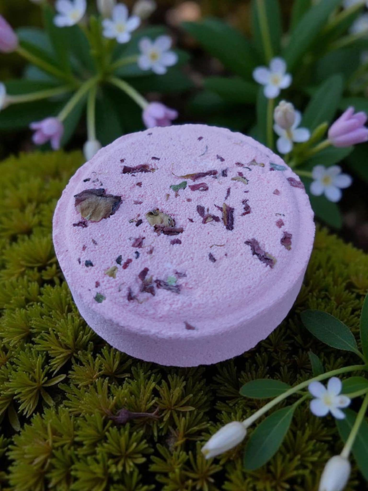 Purple bath bomb with specks on a green moss background with small white flowers