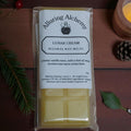 Pack of Alluring Alchemy Lunar Cream beeswax wax melts on a wooden surface with a candle and pine cone.
