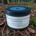 Beeswax candle labeled 'Lunar Silk' on a natural background with plants and wood.