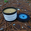 Scented candle in a tin with a label on a bed of pine needles