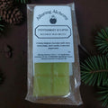 Packaged beeswax wax melts with 'Alluring Alchemy' branding on a dark background with greenery.