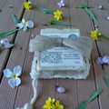 Bar of soap with a decorative bow on a wooden surface surrounded by flowers