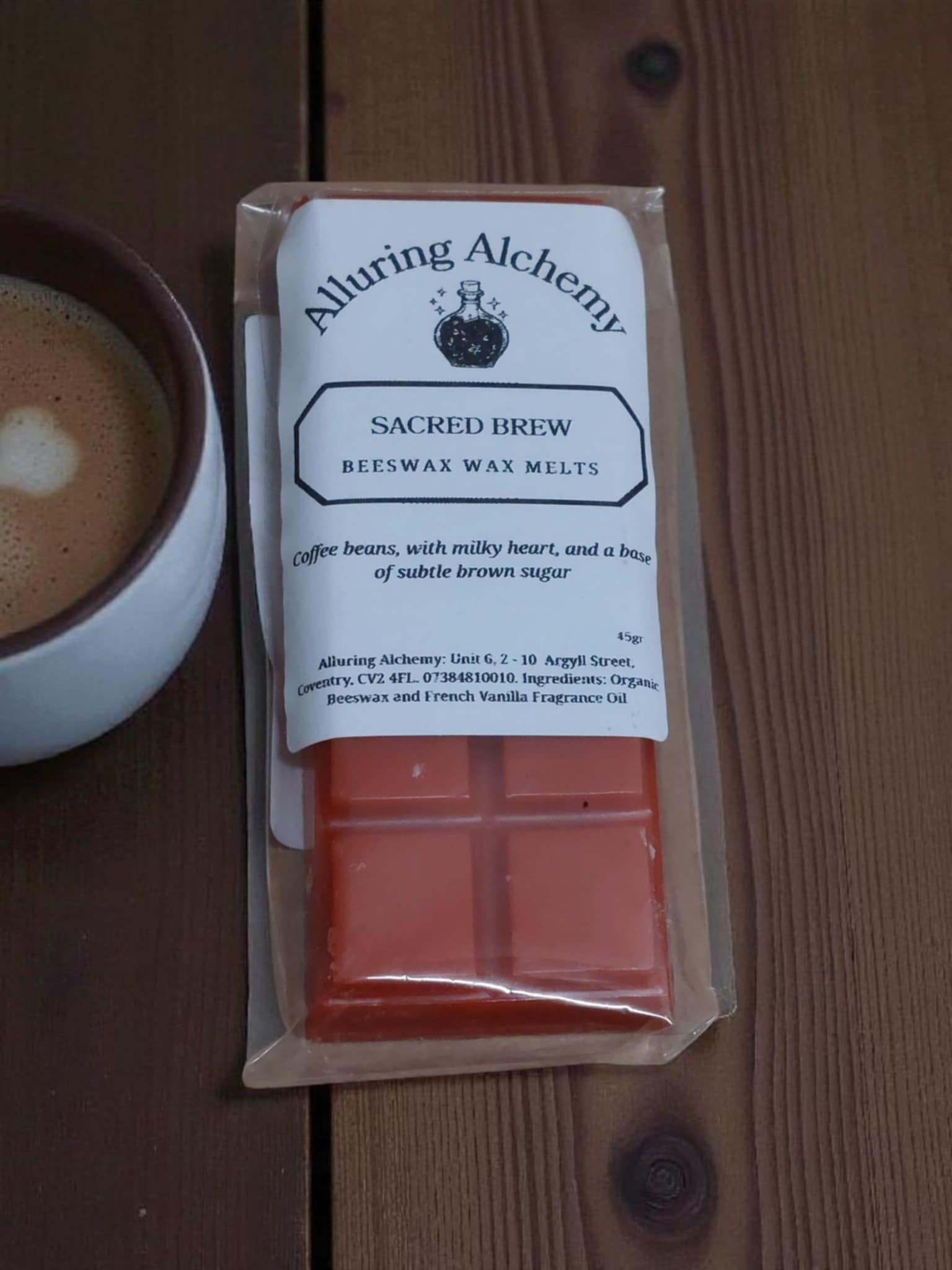 Pack of Alluring Alchemy Sacred Brew beeswax wax melts on a wooden surface with a cup of coffee.