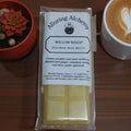 Packaged product labeled 'Alluring Alchemy' with a cup of coffee and small plant on a wooden surface.